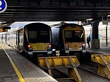2 NI Railways trains at a platform with an overhead gantry