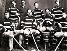 Eight young men, part of an early ice hockey team pose for a photograph, with a small silver championship trophy.