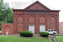 A photo of the Herron Hill Pumping Station in 2021. It is a red brick building with bricked-up windows and a white roof.