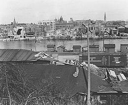 Black-and-white image showing wrecked buildings along a riverfront