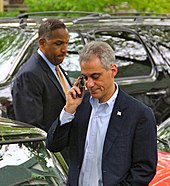 Chicago Mayor Rahm Emanuel on his cell phone, with a man standing behind him.