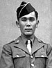 Head and shoulders of a young man standing erect, wearing a garrison cap and a military jacket over a shirt and tie.