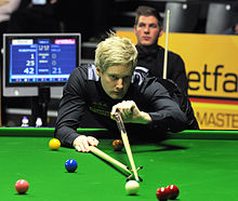 A photograph shows one man leaning over a snooker table to line up a shot while another man stands behind him watching.