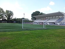 A football pitch with a goal net in the foreground, and a grandstand on the left