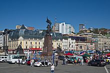A crowded city square, with cars and pedestrians