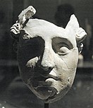A stucco mask with a high level of detail, but with missing sections and numerous cracks