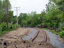 An image of newly laid railroad tracks, which end in a pile of dirt in the foreground. The tracks gradually curve to the left farther away from the viewer.