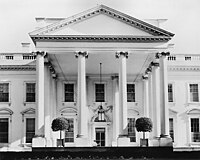 Facade of a white building with a square classical portico featuring a roof with a triangular cross-section supported by four columns on each of the three projecting sides