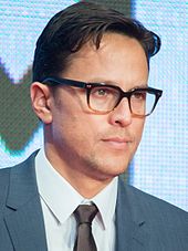 Photo of a man with short hair and glasses wearing a suit at a film premiere