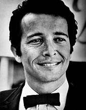 A dark-haired man wearing s tuxedo and smiling broadly