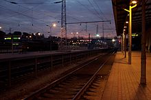 Nachtaufnahme zweier Bahnsteige mit Gleisen in der Mitte. Im Hintergrund ist ein Fußgängerüberweg. Der Bahnhof ist spärlich beleuchtet, nur rechts ist der Bahnsteig gut zu erkennen.