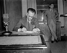 Quezon, writing at a desk behind a U.S. radio microphone