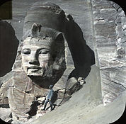 View of the rightmost statue at the Great Temple, partially excavated, with a person (possibly William Henry Goodyear) for scale