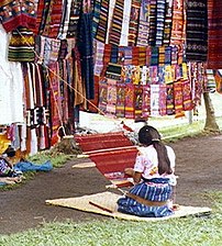 Weaving narrow cloth on a back-strap loom in Guatemala; finished narrow cloth is hung above
