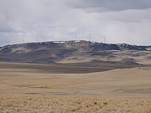 Turbines of the Gordon Butte Wind Farm sit atop the plateau, as seen from the east, with brown rolling prairie in the foreground.