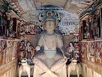 Figure of Maitreya Buddha in cave 275 from Northern Liang (397–439), one of the earliest caves. The crossed ankle figure with a three-disk crown shows influence from Kushan art. Mogao Caves