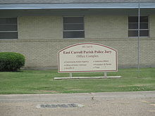 Exterior photograph of a brick government building with a prominent sign. The sign reads 402 second street East Carroll Parish Police jury Office Complex: community action agency, office of motor vehicles, section eight, veterans affairs, probation and parole, and triad.