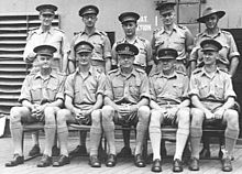 Formal group portrait of men in Army uniforms. One is wearing a slouch hat; the rest have peaked caps