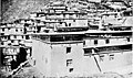 A corner of the three-storey[11] monastic print house (Derge Parkhang) in 1918, with parts of the larger monastery visible in the background above.[9]