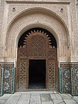 Entrance to the central courtyard adorned with cedar wood screen (mashrabiya) and carved stucco around the archway