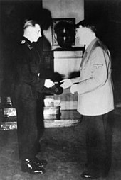 Wittmann, standing on the left, is shown receiving his Knight's Cross of the Iron Cross from Adolf Hitler standing on the right.