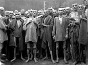 Just-liberated Ebensee concentration camp survivors wear (and some show to the camera) metal tags bearing ID numbers on cord bracelets or necklaces.