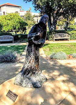 A photo of a bronze sculpture of Saint Clare leaning forward with her right hand on her heart or chest