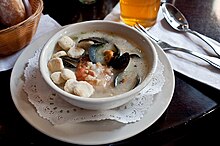A cream-style seafood chowder at a restaurant, served with oyster crackers in the bowl at left