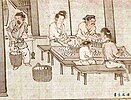 Two women, two men and a child sit at a table, sorting white cocoons in baskets.