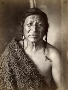 A native Crow man with braided hair wearing a think buffalo hide with fur attached over his right shoulder