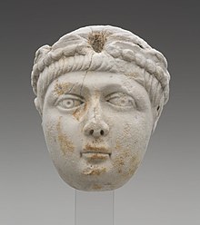 A Miniature portrait head of a a young boy with a full face and short, straight hair. He wears a pearl-edged diadem, which identifies this head as portrait of an Emperor. The head greatly resembles depictions of the Theodosian princes. This marks the identification of the head to be either Honorius, Arcadius, or Valentinian II.
