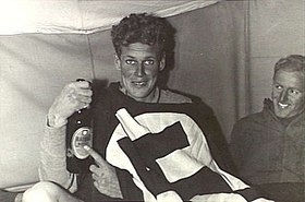 Wilfred Arthur holding a bottle of beer and grinning at the camera, in company with another grinning serviceman