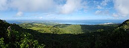 panorama of Saipan. There are green hills in the foreground, towns and beaches in the midground, sea and clouds in the distance.