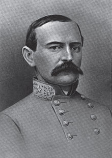 A man with receding dark hair and a full, dark mustache wearing a high-collared military jacket