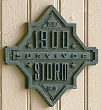 A building with a plaque reading "1900 Storm Survivor", with the year 2000 at the top and 1900 again at the bottom