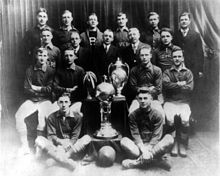 Formal team photo with two trophies and a game ball