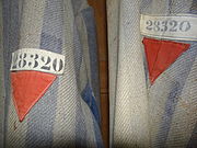 Red triangle emblems of a political enemy on a Dachau detainee's clothing. The white cloth-tape above bears the ID number 28320. ^