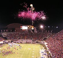 Football players enter a packed stadium with fireworks erupting at one end