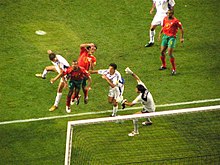 Close-up view of the penalty area and part of the goal, showing three Portuguese players and four Greek players, with Charisteas in the air heading the ball