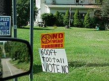 Two signs in the yard of a rural house, reading "NO Wind Turbines" and "600ft too tall VOTE NO".