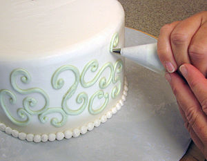Light green buttercream is piped in swirls onto a white cake.