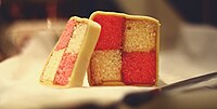 Homemade Battenberg cake covered in marzipan and, when cut in cross-section, displaying a distinctive two-by-two check pattern alternately coloured pink and yellow