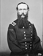 Black and white photo shows a man with a foot-long beard. He wears a dark, double breasted uniform with general's stars on the shoulder tabs.