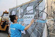 "A person with a respiratory mask and UNICEF t-shirt is touching a shipment of Covid-19 vaccines, delivered to Vietnam in 2021 as part of the COVAX advance market commitment.