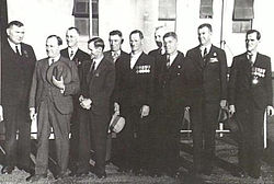 A group of ten men wearing suits and military medals gathered together outside of a building.
