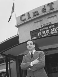 Black-and-white photo of man in a suit outside a cinema theatre with his arms folded