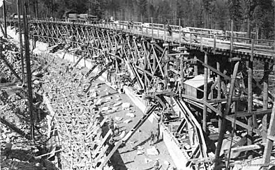 A wooden dam is pictured in a black and white photo, the dam being constructed is at Huntington Lake, CA in 1912.