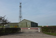 A communications mast, buildings and crash gate at RAF Barkston Heath.