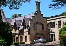 Partial view of a Gothic Revival sandstone mansion with crow-stepped gables and pairs of tall chimneys