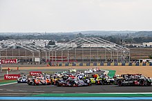 A plethora of cars turning left into a corner at the Circuit de la Sarthe